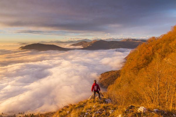 Hiker admire the panorama and clouds under him on the top of Bronzone Mount (Prealpi Orobiche). Viadanica, Bergamo province, Lombardy, Italy, Europe